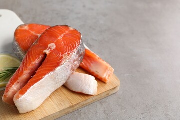 Wall Mural - Board with fresh salmon steaks, rosemary and lemon on grey textured table, closeup. Space for text