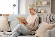 © Pixel-Shot - Young woman with short hair reading book on sofa at home