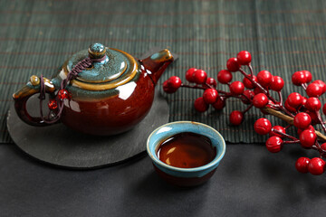 Wall Mural - Teapot with cup of tea and viburnum branch on black background