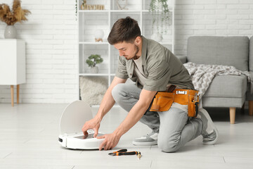 Poster - Young man with tool belt fixing modern robot vacuum cleaner at home