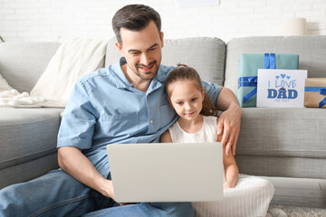 Wall Mural - Fathers and his little daughter using laptop in living room. Father's Day celebration