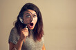© TamJam/peopleimages.com - Girl, portrait and surprise with magnifying glass in studio for investigation on bargain for price saving and retail discount. Spy, loupe and inspection with shock on background for fashion deal.