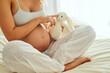 © TamJam/peopleimages.com - Teddy bear, pregnancy and woman on bed in home for prenatal bonding, connection or care with baby. Plush bunny toy, relax and pregnant female person in bedroom for maternity health at apartment.