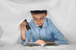 © Pixel-Shot - Teenage boy with shining flashlight reading book under blanket