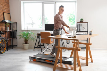 Poster - Young businessman working with tablet computer on treadmill at table in office