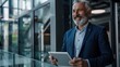 © Dzikrul Husnani - Happy middle aged business man ceo wearing suit standing in office using digital tablet. Smiling mature businessman professional executive manager looking away thinking working - generative ai