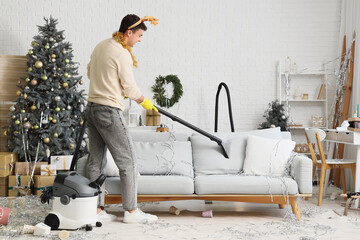 Poster - Young man vacuum cleaning sofa at home after New Year party