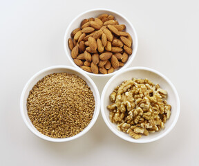 Wall Mural - Close-up and top angle view of three bowls with dried grains of flax seed, almond and walnut, South Korea
