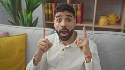 Poster - Amazed young hispanic man at home, looking up, pointing and expressing surprise with glee