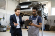 © sofiko14 - Mechanic and businessman discussing car issues in auto repair shop. Businessman looking concerned while mechanic explains report. Collaboration and communication in mechanical repair industry.