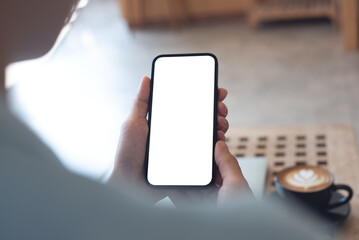 Canvas Print - Mockup, woman's hands holding mobile phone with blank screen in coffee shop. Woman using smartphone, looking at the screen, over shoulder view