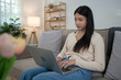 © snowing12 - Young asian women putting laptop on legs and typing business report about marketing data of new startup while sitting on the couch to spending time and relaxation with enjoying lifestyle at home
