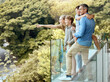 © peopleimages.com - Happy, family and and pointing on balcony, parents and bonding with children, smile and love in home. Outdoor, mom and dad with kids, hand and glasses for man, summer and woman in property and house