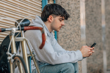 Wall Mural - urban cyclist sitting on the street with mobile phone