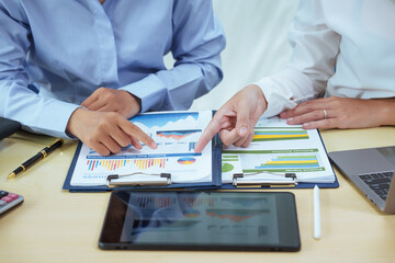 Two young Asian businesswomen sit at a table, engaged in a meeting.examine graphs and discuss capital investment strategies, showcasing their expertise and collaborative approach to business growth.