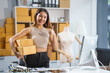 © NanSan - A young Asian businesswoman sits at a table, working on selling products online. She takes orders, packs items, and prepares shipments for customers, ready to send them to the post office.