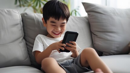 A young boy smiles while looking at his phone.