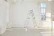© Studio Romantic - Interior with freshly painted white walls, step ladder, large plastic windows, paint bucket, piece of protective transparent film cover on floor, and no people. Home renovations, house renewal concept