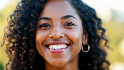 Wall Mural - A woman with curly hair is smiling and looking at the camera. She has a bright and happy expression on her face