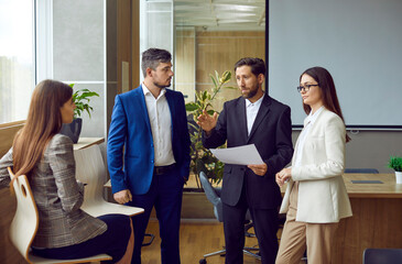 Wall Mural - Business team discussing work tasks during a corporate work meeting in the office. Group of people in formal suits talking about current business projects in a modern office workplace