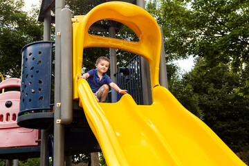 Low angle view of cute three-year old boy in casual clothes climbing on yellow slide in children playground, Montreal, Quebec, Canada 