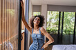 © lordn - Portrait of a young beautiful cheerful woman of African descent standing near a big sunlit window of a hotel room.
