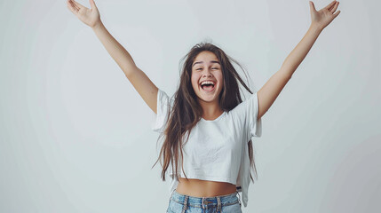 Wall Mural - A joyful young woman with arms raised in celebration, wearing casual clothes, against a plain white background, expressing excitement and happiness.