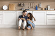 © fizkes - Young Hispanic couple resting seated on warm floor in fashionable kitchen, enjoy pleasant conversation, drinking beverage, spend relocation day to their first own house together. Cohabitation, love