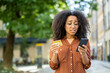 © Tetiana - Close-up photo of an upset and disappointed young African American woman standing outside on a city street and looking worriedly at a credit card and phone in her hands