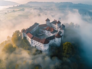 Wall Mural - An aerial view of the white castle with red roof, nestled on top of an isolated hill surrounded by dense fog and mist.