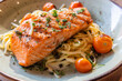 © wollertz - A plate of pasta with a piece of salmon on top. The salmon is seasoned with herbs and spices. The pasta is cooked and served in a bowl. The dish looks delicious and appetizing