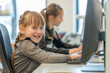 © dakinya - Happy young girl at computer, cheerful learning environment, another student focused in the background