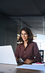 Busy 30s latin hispanic middle age business woman working on laptop computer in office. Focused Indian young businesswoman professional entrepreneur using pc application online at workplace. Vertical