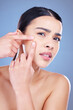 © Van Wyk/peopleimages.com - Skincare, pimple and portrait of woman in studio for cosmetics, wellness and facial treatment. Dermatology, acne and person with worry for natural skin texture, health and breakout on blue background