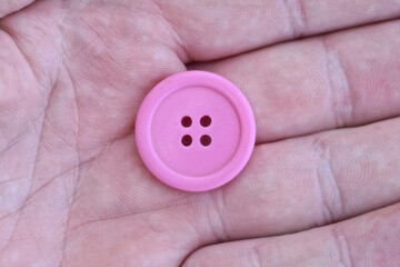 one large round plastic pink button lies on the fingers of the hand