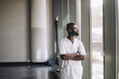 © Maskot - Mature male medical professional looking through window while standing with arms crossed at hospital