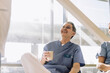 © Maskot - Smiling senior male medical expert holding coffee glass while sitting in cafeteria with colleagues