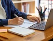 © 貴宏 西山 - A close-up of a student taking notes with a laptop, textbooks, and stationery spread out on