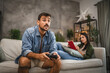 © Miljan Živković - Nervous adult man sit on sofa and play video games on joystick