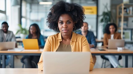 Attractive african young confident businesswoman sitting at the office table with group of colleagues in the background, working on laptop computer - generative ai