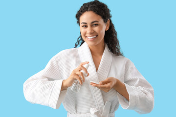 Sticker - Young African-American woman pouring makeup remover onto cotton pad on blue background