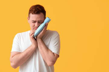 Canvas Print - Young man with hot water bottle suffering from toothache on orange background