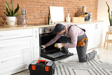 Poster - Male technician repairing electric oven in kitchen