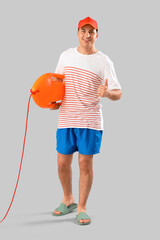 Wall Mural - Happy male lifeguard with life board showing thumb-up gesture on grey background