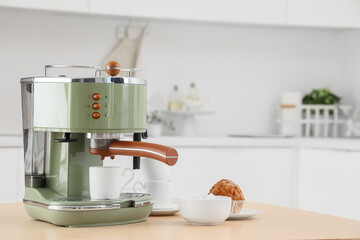 Wall Mural - Modern green coffee machine with bowl of sugar, cups and cupcake on table in kitchen