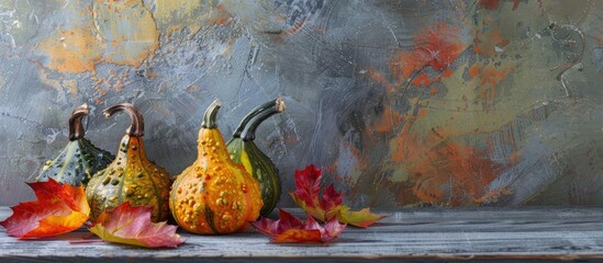 Leinwandbilder - Three gourds adorned with colorful autumn leaves sit on a textured grey wooden table with space available for text or images in the background. with copy space image. Place for adding text or design