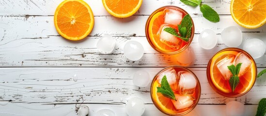 Poster - Flat lay presentation of delectable cocktails featuring vibrant orange garnish fresh mint and ice spheres on a white wooden surface with available copy space for text