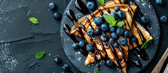 Fototapete - Chocolate crepes with blueberries sauce and mint leaves on a slate plate in a top view shot with a focused area left for text or design known as copy space image