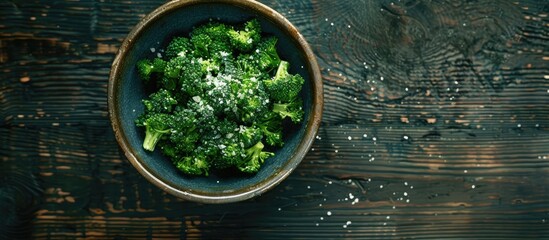 Poster - An aerial view of a bowl of sea salt topped green broccoli on a dark rustic wooden surface providing a copy space image