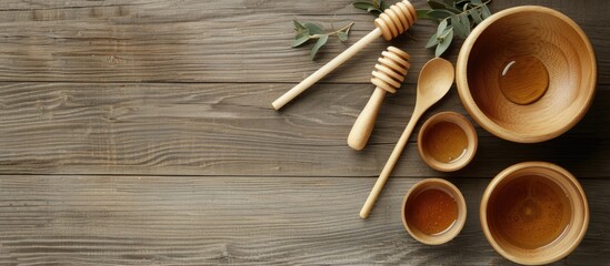 Poster - Wooden kitchen utensils like bowls spoons and a honey stick arranged on a wooden table background with three bowls a honey stick and two spoons A flat lay of wooden kitchenware showcasing a copy space